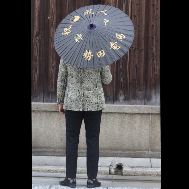 成人式の日に名前入りの和傘をさす男性の後ろ姿